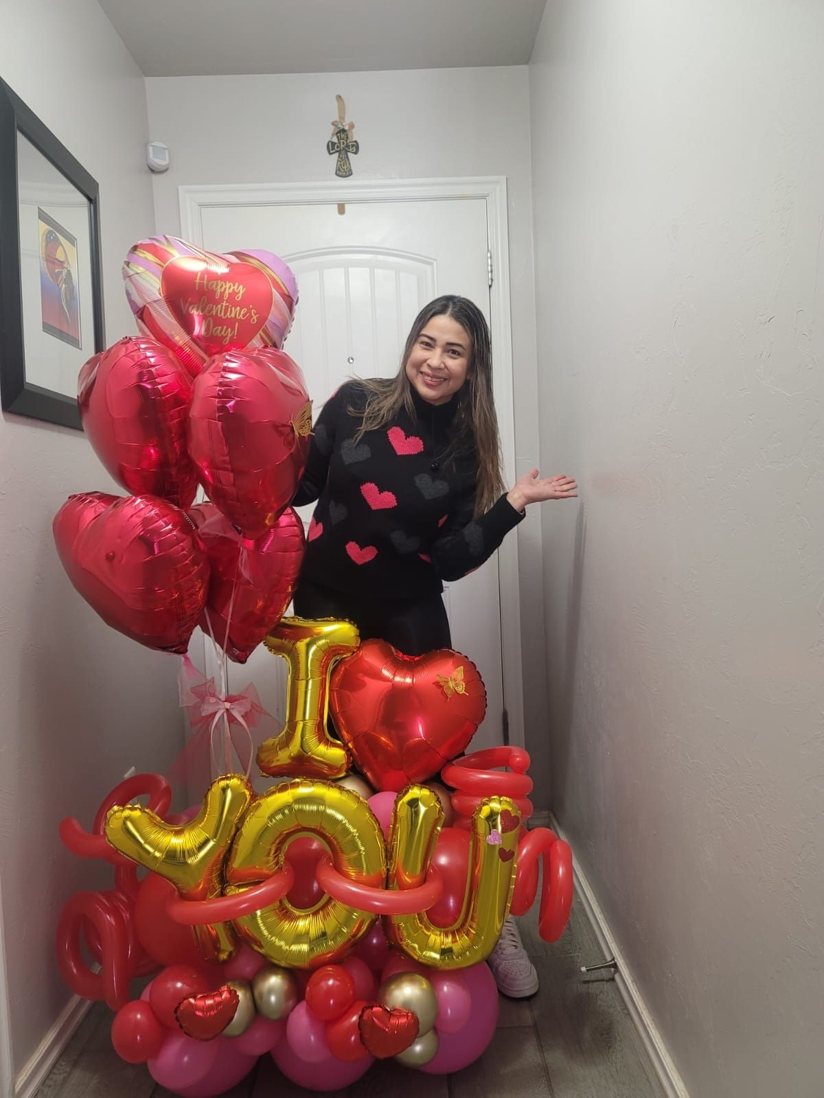 Woman smiling with heart-shaped balloons and 'I love you' balloon arrangement for Valentine's Day.