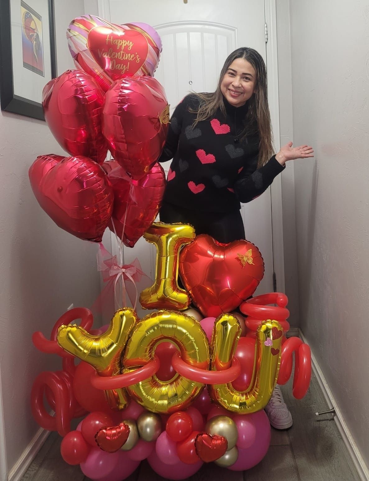 Smiling woman with Valentine's Day heart balloons and a balloon arrangement spelling 'I love you'.